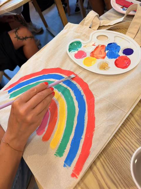 Guest painting a rainbow on a tote bag, palette beside it